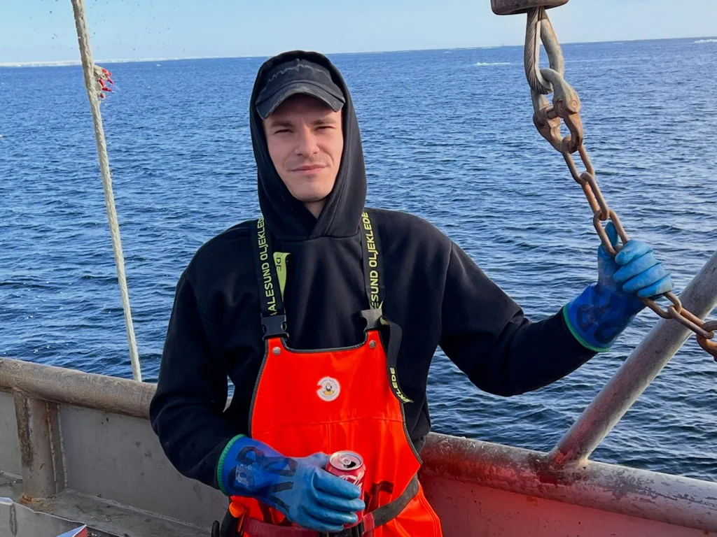 Ренат Бесолов держит шкентель подъёмного крана на палубе краболова. Весна 2022.